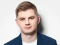 Młody mężczyzna w niebieskiej marynarce w kratę, gotowy do występu. Polski stand up w jego wykonaniu to gwarancja dobrej zabawy.