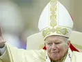 Papież Jan Paweł II w białej mitrze z haftem, pozdrawia wiernych. Jego dłoń z pierścieniem jest uniesiona. Codzienna modlitwa do św. Jana Pawła II.