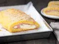 Rotolo dorato di polpettone di patate ripieno di prosciutto e formaggio filante, pronto per essere gustato.