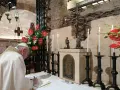 Papst Franziskus schreibt in einem Buch, während Kerzen und rote Anthurien brennen. Dies erinnert an die Bedeutung einer Enzyklika, eines wichtigen päpstlichen Schreibens.