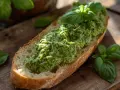 Fetta di pane croccante con abbondante pesto di zucchine e basilico fresco, su tagliere di legno.