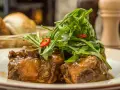 Delicioso rabo de toro en salsa, coronado con rúcula fresca y rodajas de chile. Una receta que conquista paladares.