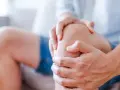 Mężczyzna trzyma się za kolano, odczuwając rwący ból kolana w spoczynku.