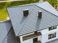 Nowoczesny dom z szarym, czterospadowym dachem z blachodachówki. Dwa kominy wystają ponad linię dachu.