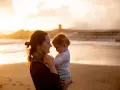 Matka tuli dziecko na plaży o zachodzie słońca. Ciepłe światło podkreśla ich bliskość, ale pamiętaj, **dlaczego z gorączką nie można iść na dwór** – dla zdrowia malucha.