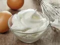 Zwei Eier und ein Schneebesen neben einer Schüssel mit luftigem Eischnee, der nicht fest wird.