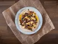 En krämig aubergine i ugn serveras på en bädd av hummus, toppad med en smakrik blandning av oliver, kapris och örter.