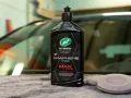 En flaska Turtle Wax Hybrid Solutions Pro Graphene Infused To The Max Wax står på en grå trasa bredvid två appliceringsdynor.