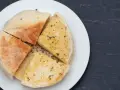 Pokrojone na ćwiartki bolo do caco, posypane ziołami, na białym talerzu.