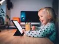 Uśmiechnięta dziewczynka ogląda ulubionych youtuberów dla dzieci na tablecie.