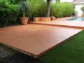 Une belle terrasse en béton coloré ocre, idéale pour un devis terrasse béton. Entourée de verdure et d'une piscine.