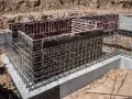 Siatka zbrojeniowa otacza betonowe szalunki, tworząc solidne zbrojenie ściany fundamentowej.