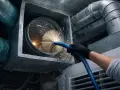 Persona con guantes negros usa cepillo para limpiar conductos de aire acondicionado.