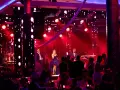 Sylwester w Hotelu Gołębiewski: zespół na scenie, wokalistka w fioletowej sukni, muzycy i publiczność bawią się przy czerwonych światłach.
