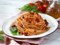 Un piatto di spaghetti conditi con un sugo rosso ricco di pomodori secchi, basilico fresco e un filo d'olio d'oliva.