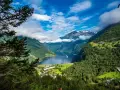Majestatyczne fiordy Norwegii, z zielonymi zboczami gór, błękitnym niebem i statkiem wycieczkowym na wodzie.