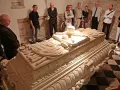 Grupa zwiedzających ogląda kamienny sarkofag w wawel krypty. Kamienne rzeźbienia zdobią jego bok.