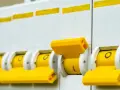 Rząd żółtych dźwigni wyłączników nadprądowych, pokazujący różne rodzaje bezpieczników w akcji.