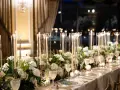 Eleganckie kwiaty na wesele zdobią stół, a wysokie świece w szklanych wazonach tworzą magiczny nastrój.