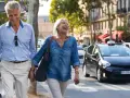 Uśmiechnięta para seniorów spaceruje po mieście z walizką, obok przejeżdżają samochody.