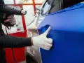 Ein Handwerker erwärmt mit einem Heißluftföhn eine blaue Folie, die auf ein Auto aufgebracht wird. Die auto folieren kosten sind hierbei ein wichtiger Faktor.