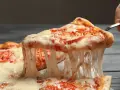 Rozciągający się, ciągnący ser na kawałku pizzy z pomidorami. Idealny przykład, jaki ser do pizzy wybrać, by uzyskać taki efekt.