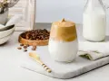 En krämig dalgona coffee med fluffigt skum, serverad med mjölk och kaffebönor.