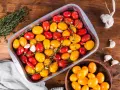 Pomodorini al forno rossi e gialli, aglio e peperoncino in una teglia, pronti per essere cotti.