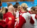 Drużyna piłki ręcznej w czerwonych strojach, zjednoczona przed meczem. Emocje i determinacja na twarzach zawodniczek podczas mistrzostw świata.
