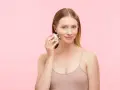 A woman demonstrates how to use a face massager on her cheek, showing a simple skincare routine.