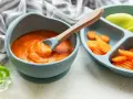 Karottenpüree und geschnittene Karotten auf einem Baby-Teller, bereit für leckere Beikost-Rezepte. Ein Löffel mit Püree ist in der Schüssel.