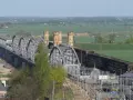 Imponujący most w Tczewie, z charakterystycznymi wieżyczkami, przecina rzekę na tle zielonych pól i drzew.