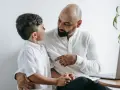 Ojciec z synem rozmawiają o tym, jak przyspieszyć tempo pracy dziecka. Ojciec wskazuje palcem, syn słucha uważnie.