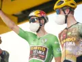 Cyclist in a green jersey, the symbol of the points classification leader at the Tour de France, raises his arm. He wears a mask and helmet.