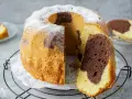 Saftiger Marmorkuchen, perfekt gebacken mit Ober-/Unterhitze oder Umluft, bestäubt mit Puderzucker. Ein Stück ist bereits angeschnitten.