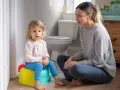 Mama uczy dziecko korzystać z nocnika. Mała dziewczynka siedzi na kolorowym nocniku, a mama siedzi obok, wspierając ją.