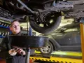 Mechanik wymienia olej w samochodzie, trzymając miskę z zużytym płynem.