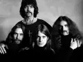 Czarno-białe zdjęcie zespołu Black Sabbath. Czterech mężczyzn z charakterystycznymi fryzurami i wąsami pozuje do portretu.