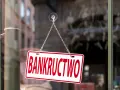 Tabliczka "BANKRUCTWO" wisząca na łańcuszku na szybie.