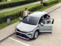 Jasnoszary elektryczny SUV Škoda Elroq z otwartymi drzwiami, obok którego stoją młoda kobieta i mężczyzna.