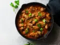 Serca drobiowe w gęstym sosie pomidorowym, udekorowane świeżą natką pietruszki, podane w żeliwnej patelni.
