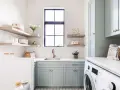 Stylish laundry room with mint cabinets, floating shelves, and a sink. This organized space shows how to organize laundry room with baskets and jars.