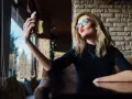 Kobieta w okularach robi sobie selfie, wyciągając usta do pocałunku. W jej spojrzeniu widać pewność siebie, graniczącą z narcyzmem.