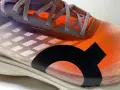 La tomaia di una scarpa da corsa arancione e viola con lacci grigi e un logo nero.