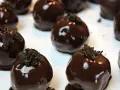 Deliziosi tartufini al cocco ricoperti di cioccolato fondente lucido, guarniti con briciole croccanti.