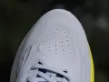 Zbliżenie na jasnoszarą, teksturowaną cholewkę buta sportowego z widocznymi perforacjami i sznurówkami.