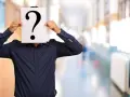 Un homme en chemise bleue cache son visage derrière un point d'interrogation. Une métaphore visuelle pour la quête : comment retrouver une personne sans son nom et prénom ?