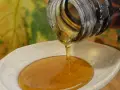 Ahornsirup tropft aus einer Flasche auf einen Holzlöffel. Die Frage, ob kann ahornsirup schlecht werden, beschäftigt viele.