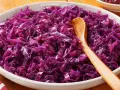 Col lombarda cocinada en un cuenco blanco con una cuchara de madera.