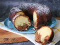 Saftiger weltbester Marmorkuchen, mit Puderzucker bestäubt, auf blauem Teller. Ein Stück ist abgetrennt und zeigt die köstliche Marmorierung.